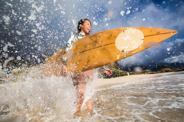 Woman gets sprayed with water from an incoming wave while into the ocean with her surfboard