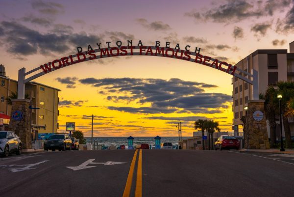 Arched sign reading "Daytona Beach - World's most famous beach" with a bright yellow sunset and the ocean in the background