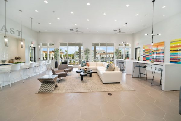 Bright, white clubhouse interior with ample seating options including countertop barstools, couches, and armchairs. all with a view of the pool through the large windows.